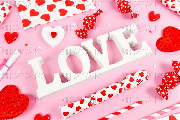 White Valentine's Day decoration LOVE text surrounded by seasonal decoration on pink background