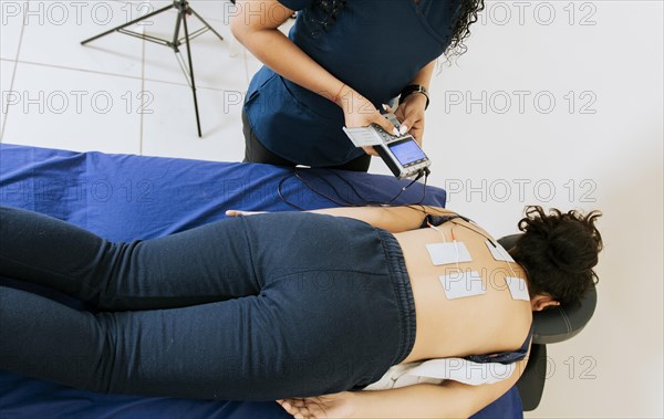 Professional physiotherapist electrostimulating a lying patient