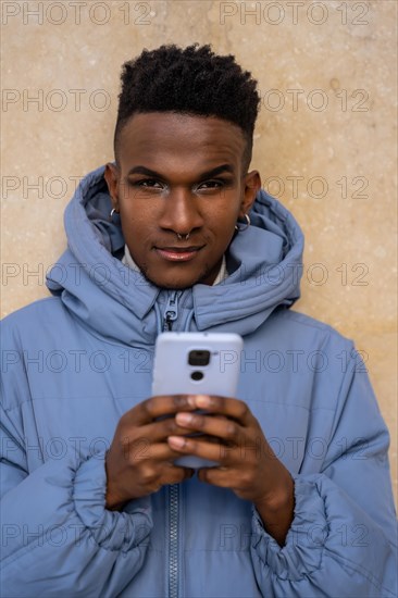 Portrait of a black ethnic man with a phone and a blue jacket on a yellow background