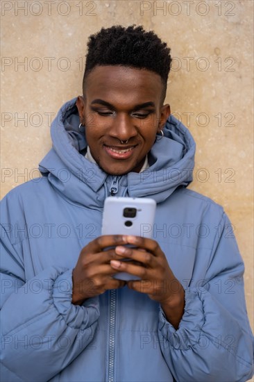A man of black ethnicity with a phone and a blue jacket on a yellow background