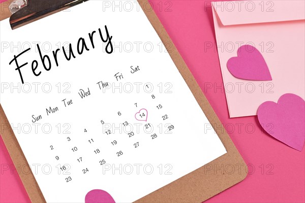 February calendar sheet with Valentines Day on the 14th marked with heart surrounded by hearts and love letter on pink background