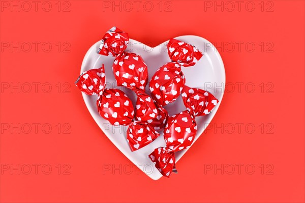 Candy wrapped in paper with hearts in bowl on red backgroun