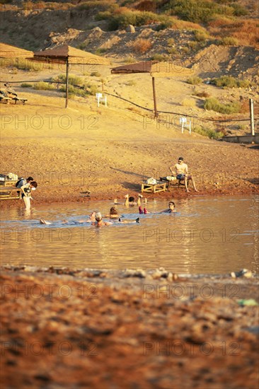 Sandy beach beach and bathers at sunset at the Dead Sea