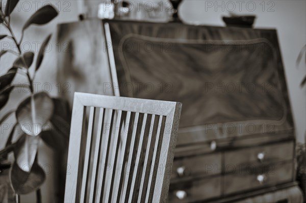 Interior shot of a beechwood chair back transitioning from sharpness to blur with an out-of-focus antique secretary in the background