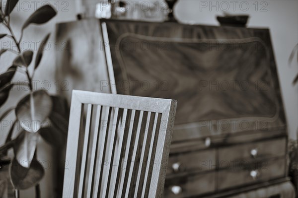 Interior shot of a beechwood chair back transitioning from sharpness to blur with an out-of-focus antique secretary in the background