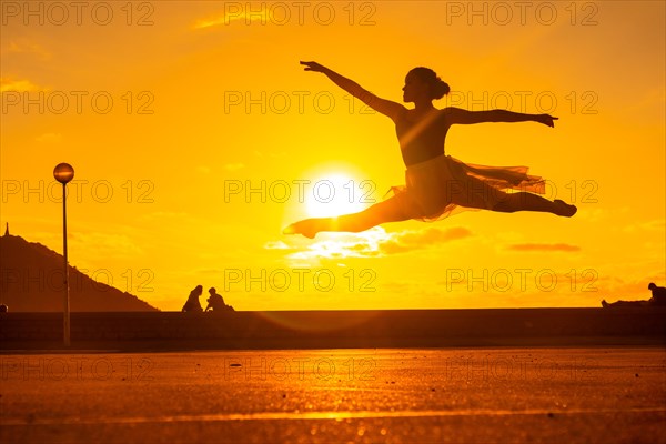Silhouette of a young female dancer performing a jump along the beach at sunset
