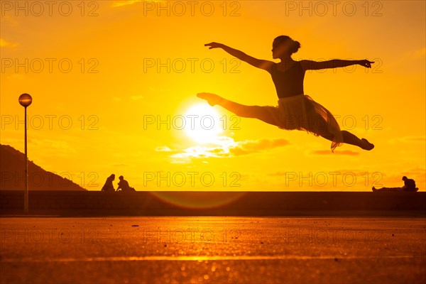 Silhouette of a young female dancer performing a jump along the beach at sunset