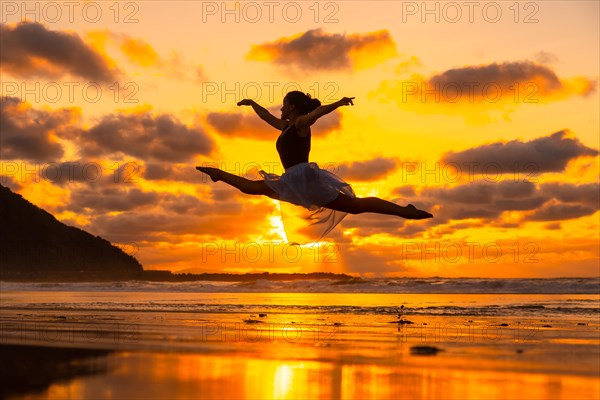 Young dancer on the beach at sunset performing a jump with the sea in the background