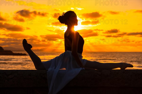 A young woman dancer by the beach at sunset doing spagata with the sea in the background