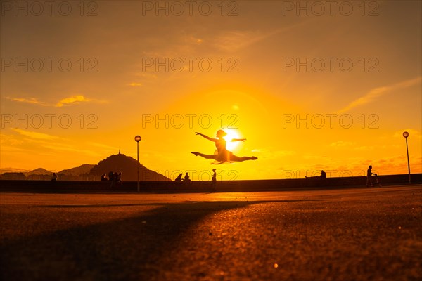 Young woman dancer performing a jump along the beach at sunset