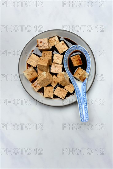 Soy sauce marinated tofu cubes in bowl with Asian ceramic spoon