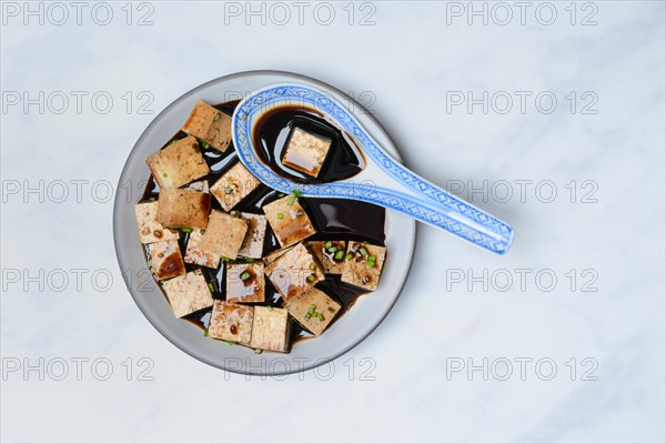 Soy sauce marinated tofu cubes in bowl with Asian ceramic spoon