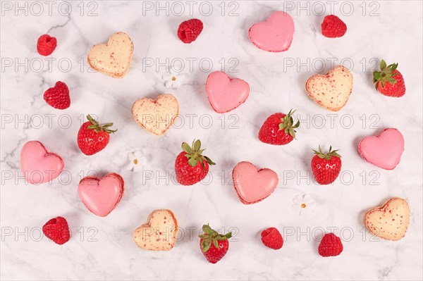 Heart shaped pink and beige French macaron sweets next to strawberry and raspberry fruits