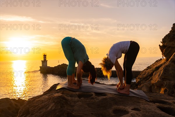 Two women stretching for meditation and yoga in nature by the sea at sunset