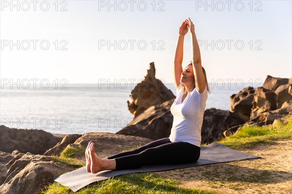 A blonde woman doing yoga exercises in nature by the sea