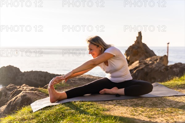 A blonde woman doing yoga exercises in nature by the sea