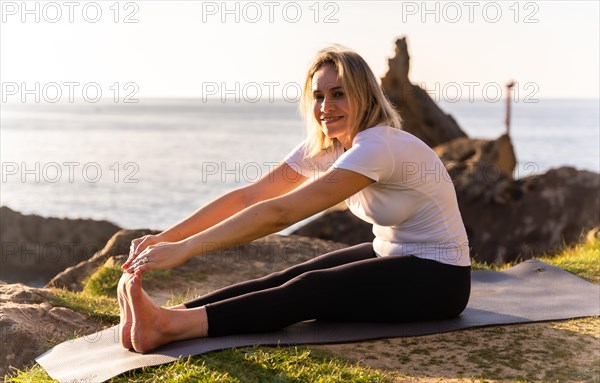 A blonde woman doing yoga exercises in nature by the sea