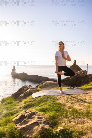 A blonde woman doing yoga exercises in nature by the sea