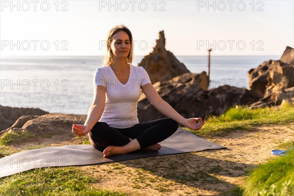 A blonde woman performing yoga exercises in nature by the sea