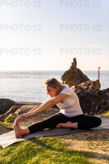 A blonde woman doing yoga exercises in nature by the sea