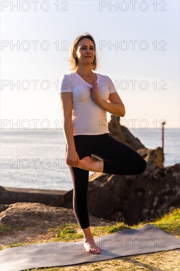 A blonde woman doing yoga exercises in nature by the sea