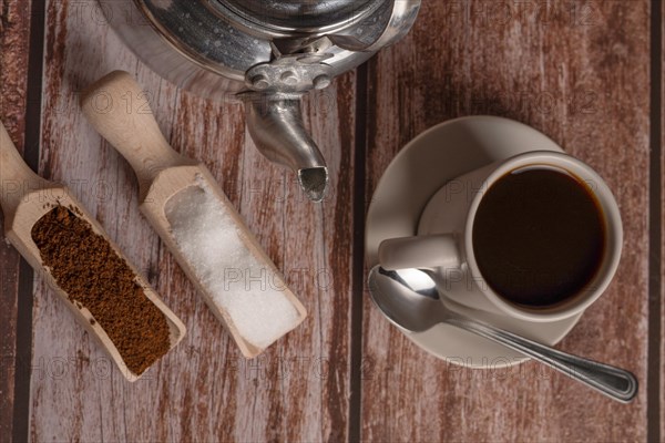 Zenithal view of a coffee cup with milk jug and wooden spoons on a wooden table with text space