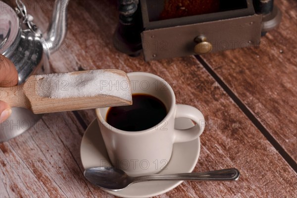 Pouring sugar into the coffee with a wooden spoon on a wooden table