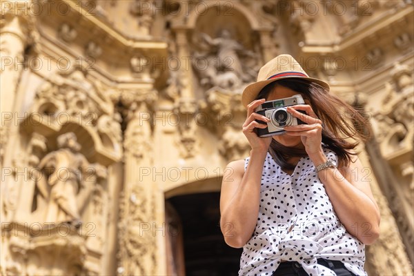 A woman in a hat visiting the city and taking photos with a vintage camera