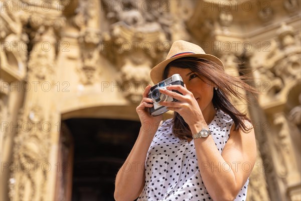 A woman in a hat visiting the city and taking photos with a vintage camera