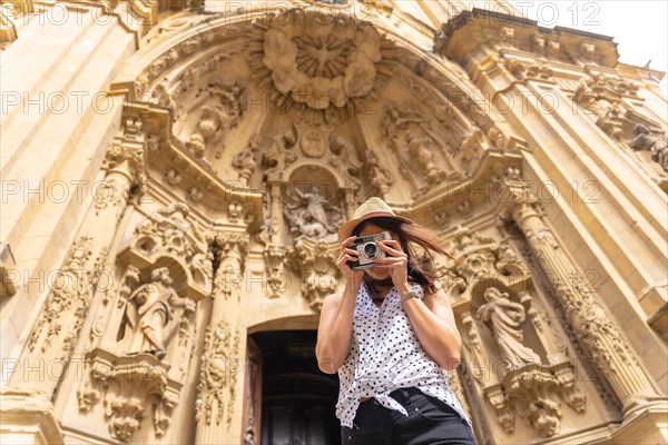 A woman in a hat visiting the city and taking photos with a vintage camera