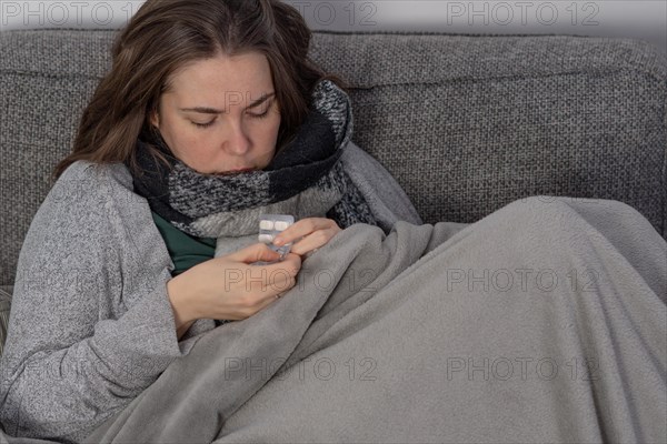 Sick woman taking fever pills covered with a blanket on the sofa in her home