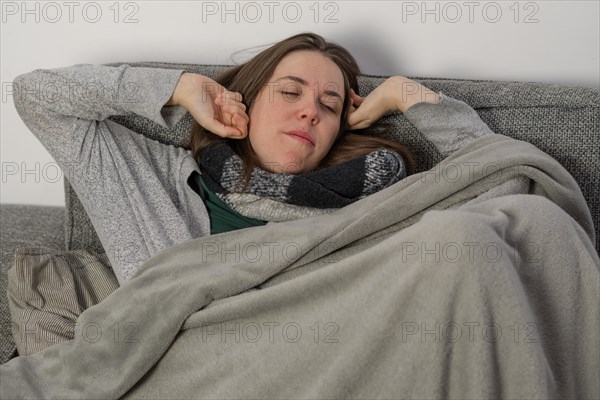 Woman waking up from a nap on the couch at home covered with a blanket and scarf