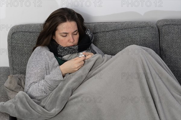 Sick woman taking fever pills covered with a blanket on the sofa in her home