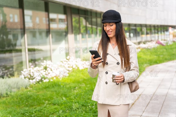 Businesswoman outside the office with a coffee in her hand and sending a text message