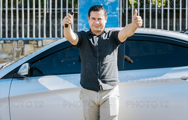 Male driver standing next to the car showing the keys with thumb up