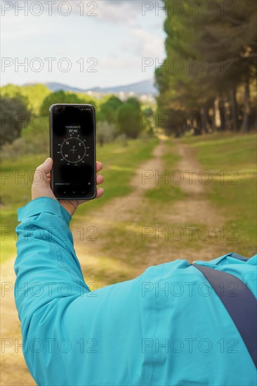 Woman orienting herself in the forest with her smart phone's compass following a trail in the pine forest