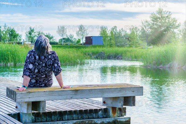 Woman sitting on a bench on a lake dock looking at the blue sky