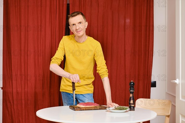 Middle-aged man leaning against knife and going to prepare duck breast