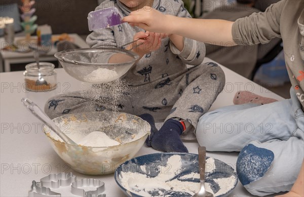 Children adding flour to a large sieve for a cake mixture