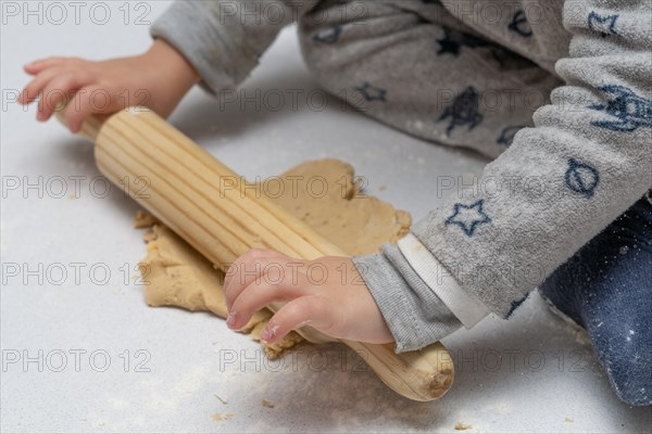 Boy kneading cookie dough with a wooden rolling pin and his brothers and mothers hands in the background