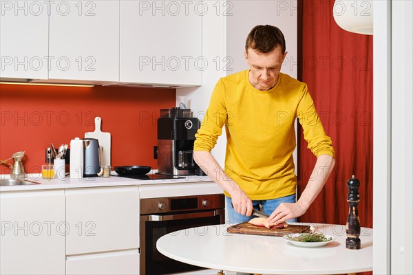 Middle-aged man cuts the skin crosswise on a duck breast in the kitchen