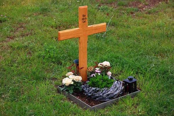 Flower decorated anonymous urn grave with wooden cross with inscription Here rests in God