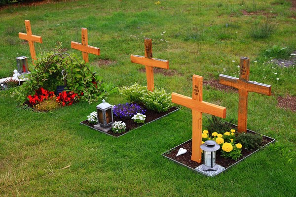 Flower decorated anonymous urn graves with wooden cross with inscription Here rests in God