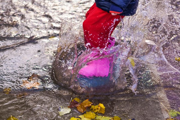 Child splashing water with boots and water pants in a puddle on a rainy day