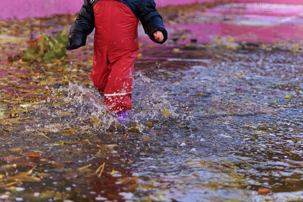 Child splashing water with boots and water pants in a puddle on a rainy day