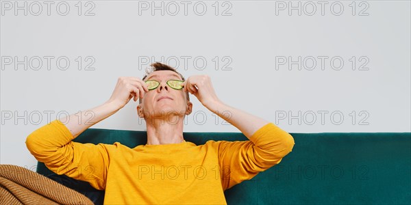 Senior man relaxing on sofa with slice of cucumber on eyes