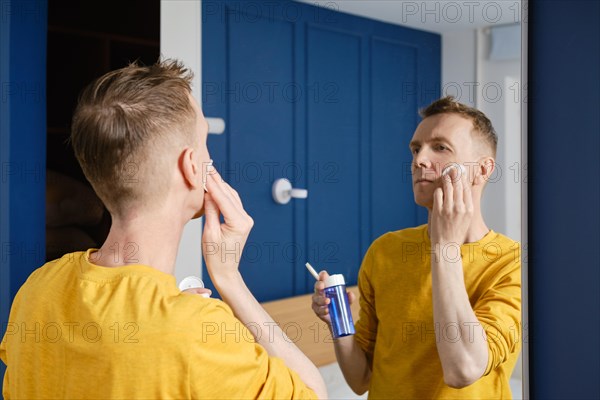 Middle aged man cleaning face with lotion using cotton pad
