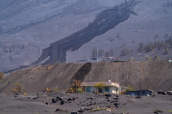 Damaged house in front of the new volcano Tajogaite at the visitor centre Canos de Fuego