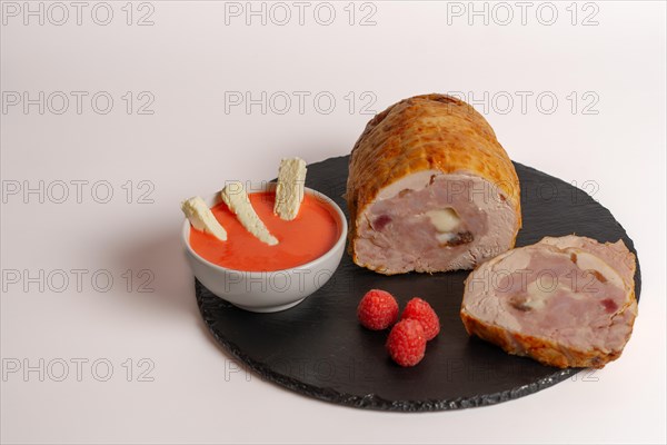 Close-up of a chicken stuffed with raspberry and goat cheese with a bowl of raspberry sauce isolated on white background