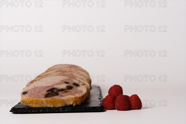 Close-up of a chicken stuffed with raspberry and goat cheese with a bowl of raspberry sauce isolated on white background